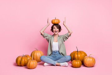 Full size photo of cheerful pretty girl sit put pumpkin on head toothy smile isolated on pink color...