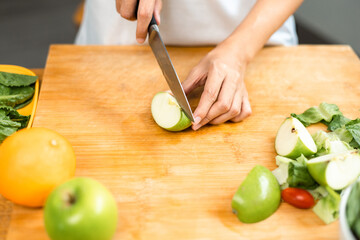 Hand of slicing and cooking green apple on cutting board for vegetable salad in weight loss diet. Beautiful woman happily cooks a healthy breakfast in kitchen in the morning. Diet food concept.