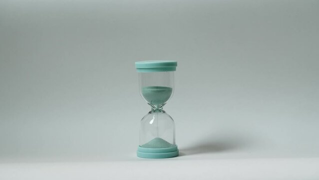 Glass hourglass with turquoise sand on isolated background