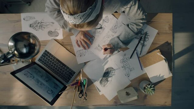 Young female illustrator drawing pencil sketches on paper. Drawings on the sheet of papers in front of her. Illustration animation, storyboard, video game film production, animation design studio.