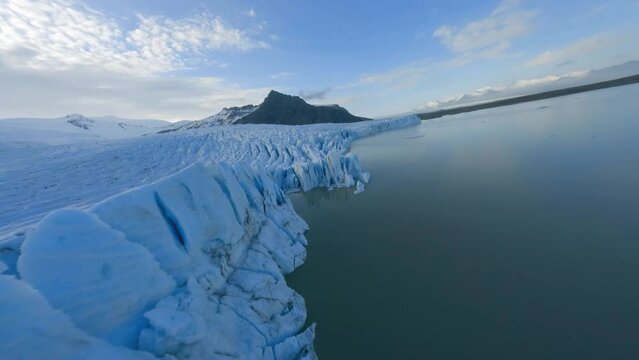 FPV drone shot flying parallel to a glacier wall, sunset in Vatnajokull, Iceland