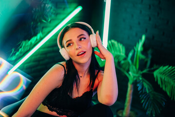 Fashion pretty woman with headphones listening to music over neon background at studio.