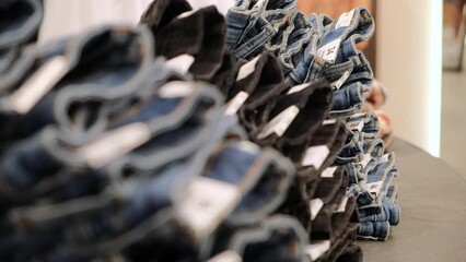 Close-up of a huge range of jeans in different sizes and styles for men and women in a large clothing store. Jeans are neatly folded and stacked. Each pair has a size tag.