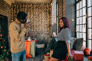 Cheerful young man and woman taking photo at home decorated for Christmas winter holiday. Happy family training together