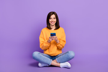 Full body photo of young adorable businesswoman sitting chilling using her smartphone successful influencer isolated on violet color background