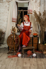 a girl in a Russian costume sits on a chest in a hut
