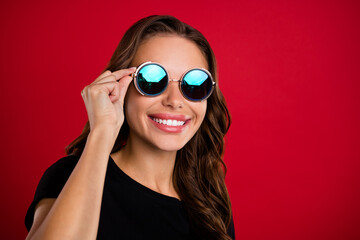 Photo of adorable charming young woman wear black t-shirt arm dark eyewear looking empty space smiling isolated red color background