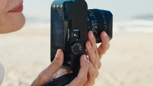 Female photographer. Brunette woman takes pictures on the beach with mirrorless camera