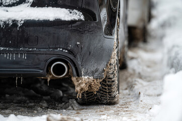 closeup rear view of a dark car on parking, dirty rear wheel tire on snow