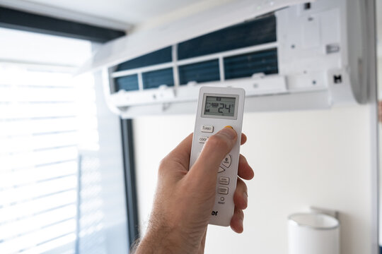 A man's hand holds a remote control from an air conditioner with a temperature on the screen of 21.
