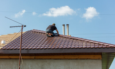 Workers install metal roofing on the wooden roof of a house.
