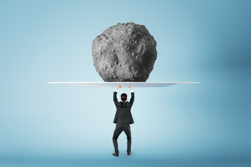 Success, power and strength concept with businessman back view holding huge stone. above his head,...