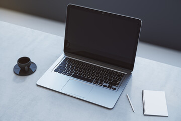 Close up of empty laptop on concrete desktop with coffee cup, notepad, pen, mock up place on screen, blurry background. 3D Rendering.