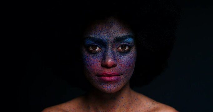 Face paint, art and makeup on black woman with afro in dark studio with unique, creative and fantasy cosmetics on skin. Glowing girl model with colorful splash, creativity and explosion of color
