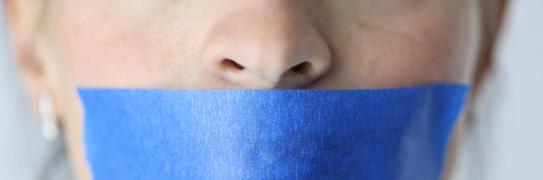 Woman mouth is sealed with blue tape closeup