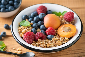 Crunchy oat honey granola with berries and fruits in bowl over wooden table background, closeup view