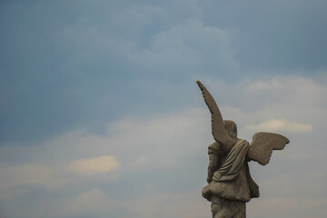 Stone sculpture of a winged angel against an ominous sky, back view. Copy space.