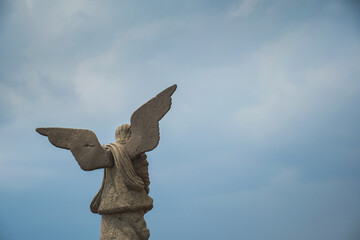 A stone statue of an angel with wings on the background of a cloudy sky. Back view. Cholula,...
