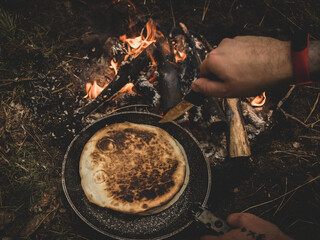 man with a knife prepares a qurrito over a fire in the woods