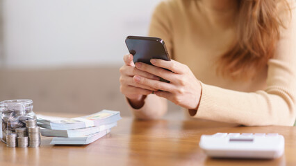 Saving money concept, Asian woman use smartphone and reading data after count the amount of savings
