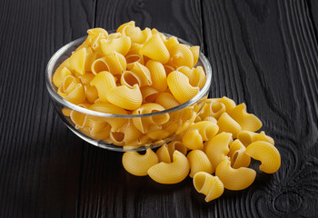 Uncooked pipe rigate pasta in glass bowl on black wooden background