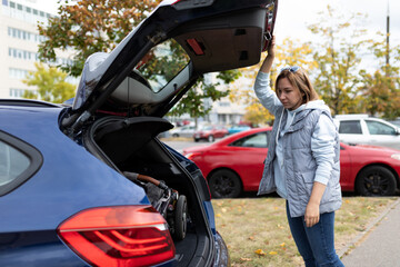 a young woman mother loaded a baby stroller into the car and stands near the trunk of the car