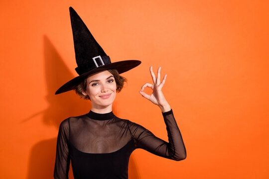 Photo portrait of nice young girl smiling show okey sign feedback wear stylish black halloween witch clothes isolated on orange background