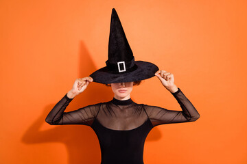 Photo of confident serious young lady wear black witch dress hands cap isolated orange color background