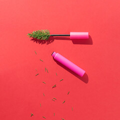 Christmas tree branch with pink mascara and fir needles on pink background. Minimal winter holidays make up concept. Creative New Year celebration aesthetic. Flat lay.