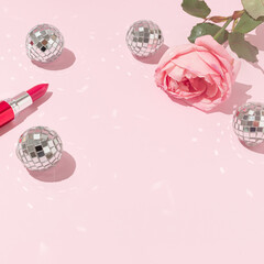 Romantic composition of pink rose flower, red lipstick and disco balls on bright pink background. Retro 70s, 80s or 90s aesthetic.