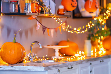 large orange pumpkin, lying on wooden table against background decorated Halloween kitchen with garland lights. Blurred background. Autumn background of Thanksgiving greeting card. Space for copying.