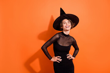 Photo of adorable funky lady wear black witch dress cap smiling laughing empty space isolated orange color background