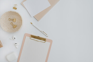 Flatlay of stylish female accessories and office stuff. Comfortable home office workspace. Work at home. Clipboard, clips, wireless headphones pen on table