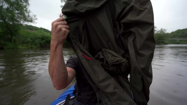 A Kayaking Man With A Beard And Dirty Face Putting On A Raincoat In The Rain