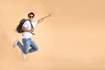 Young Asian tourist backpacker man smiling and jumping isolated on beige background