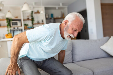 Fototapeta premium Senior elderly man touching his back, suffering from backpain, sciatica, sedentary lifestyle concept. Spine health problems. Healthcare, insurance