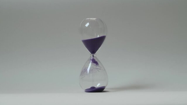 Close up of the sand clock with purple sand running down on the white wall background. Macro shooting