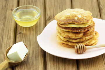 Stack of pancakes, honey and spoon with butter on wooden table