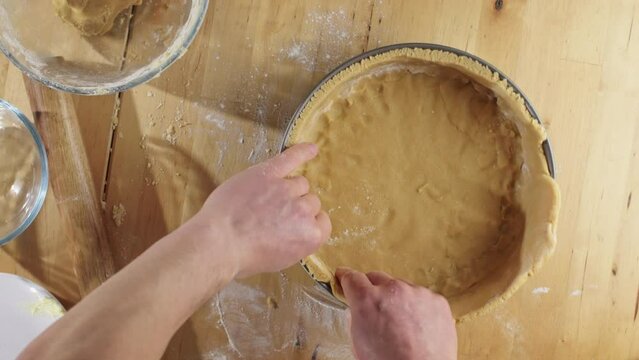 A male home chef making traditional Dutch apple pie - shaping dough in a baking form.