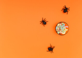 Some black spider toys and a bowl full of candy. Orange background
