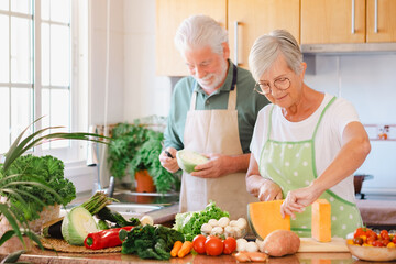 Attractive senior couple working together in home kitchen preparing vegetables. Caucasian elderly...