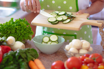 Close up on woman's hands holding a cutting board with sliced zucchini. Fresh raw vegetables on the table for a healthy eating