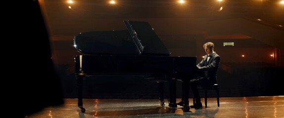 Young 20s aspiring musician playing grand piano on a stage of a huge concert hall