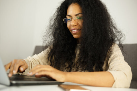 Happy black woman typing text on computer. Cheerful dark skinned female working on laptop at home. Download royalty free image of African entrepreneur person doung work. Stock photo of freelancer