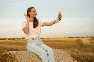 Woman makes a video call on the phone while sitting on a haystack.