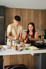 Two young hispanic people mashing potatoes and grating tomato at kitchen.