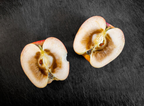 Rotten inside of an apple, cut in half and resting on top of dark cutting board.
