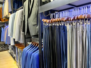 Obraz premium A collection of elegant men's suit jackets and trousers hanging in a row in a men's fashion store. 