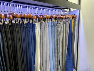 A collection of elegant men's trousers and casual pants hanging in a row in a men's fashion store