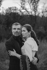 Vampire woman wearing in a burgundy coat holding lantern in autumn forest. Victorian style vintage. White and black photo